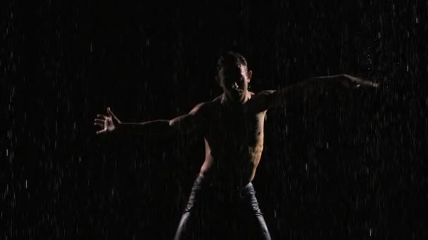 Mann mit nacktem Oberkörper bewegt sich und tanzt sexuell. Der nasse athletische Körper ist mit glänzenden Wassertropfen bedeckt. Silhouette auf schwarzem Hintergrund unter Regenströmen mit Studiolicht. Aus nächster Nähe. Zeitlupe. — Stockvideo