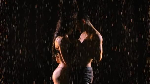 Passionerade unga par dansar och njuter av att hälla regn på natten. Silhuetter av nakna kroppar i droppar vatten. Mannen smeker försiktigt sin flickvän. Närbild. Långsamma rörelser. — Stockvideo