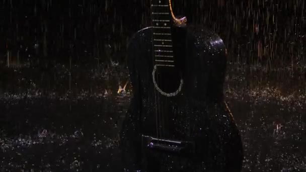 Detailní záznam dřevěné akustické kytary v dešti. Kapky vodního bubnu na povrchu kytary roztroušené v různých směrech na černém pozadí studia. Zavřít. Zpomalený pohyb. — Stock video