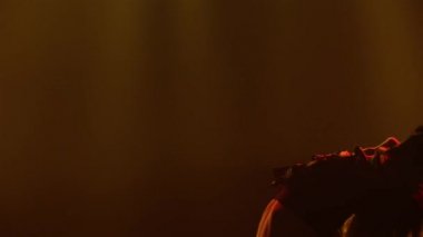 Çingene kostümlü tutkulu bir kadın dans ediyor ve uzun eteğini sallıyor. Sarı ışığı olan karanlık dumanlı bir stüdyoda bir dansçı çingene halk dansında siluete bürünür. Kapat..