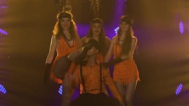 30 'lardan kalma Şikago tarzı kostümlü dans grubu stüdyoda parlak ışıklarla neşeyle dans ediyor. Şapkalı bir adam ve kısa elbiseli bir kadın partide tiyatro gösterisi yapıyorlar. Kapat..