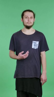 Adam kameraya bakıyor, şaşırmış bir şekilde kim olduğumu gösteriyor, kollarını sallıyor ve başını sallıyor, hayır teşekkürler. Stüdyoda yeşil ekranda bir adamın portresi. Ağır çekim. Dikey video.