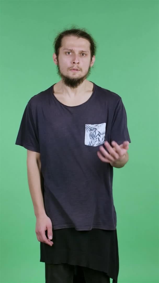 Portrét mladého muže, který se netrpělivě dívá do kamery, mává rukama a pak zaťatými pěstmi. Muž ve studiu na zelené obrazovce. Zpomal. Svislé video. — Stock video
