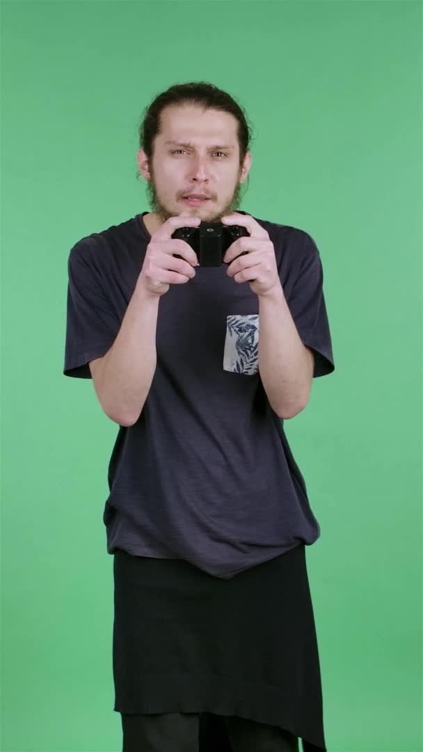 一个紧张的年轻人用无线控制器玩电子游戏的肖像，为游戏的胜利而高兴。一个男人在工作室的绿色屏幕上。慢动作垂直录像. — 图库视频影像