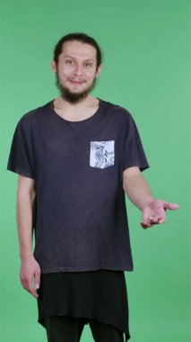 Bir adam mutlu bir şekilde gülümsemeye başlar, avuçlarını kaldırıp ellerini kaldırır. Stüdyoda bir adam yeşil bir ekranın arka planına karşı, bir kroma anahtarı. Beklenmedik bir toplantı. Ağır çekim. Dikey video.