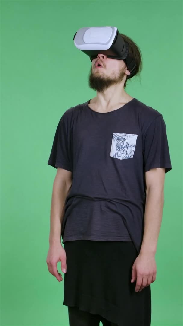 Portret van een jongeman met een virtual reality headset of 3d bril op zijn hoofd. Een brunette met een baard en een zwart shirt in de studio op een groen scherm. Langzame beweging. Verticale video. — Stockvideo