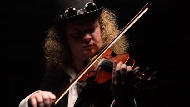 O retrato do homem em um chapéu original no estilo irlandês toca violino no fundo preto. O violinista manipula magistralmente o arco do violino, tocando cordas no estúdio escuro, iluminado por luzes brilhantes. Fechar — Vídeo de Stock