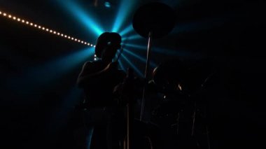 Bateri ve perküsyon zilleri çalan bir rock müzisyeninin alt görüntüsü. Davulcu, havalı bir canlı rock konseri yaratmak için bagetlerin ustasıdır. Işık huzmesinin merkezinde bir siluet.