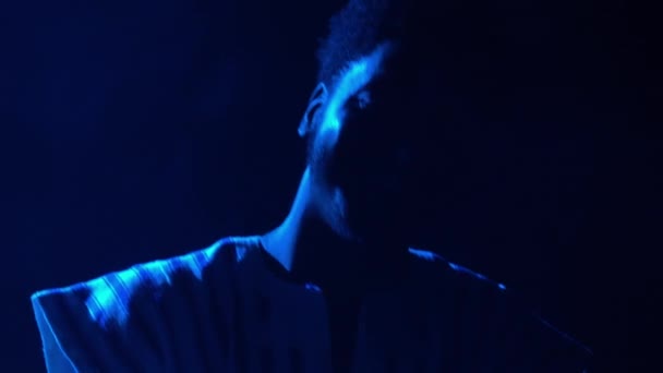 Silhouette di uomo afroamericano che suona il sintetizzatore di pianoforte sul palco in uno studio fumoso buio. Musicista nero con motivo etnico bianco sul viso si esibisce sullo sfondo di luci blu. Da vicino.. — Video Stock