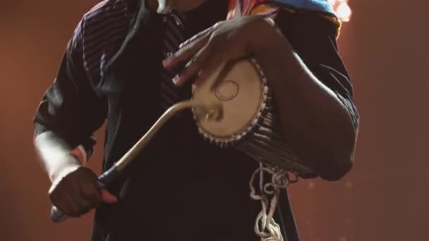 Svart musiker spelar talande afrikansk yuka trumma i en mörk studio mot bakgrund av starkt ljus. En afroamerikan slår på trumman och njuter av musiken. African National Folklore. Närbild. — Stockvideo