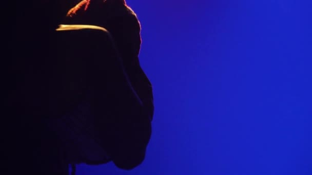 Африканская этническая музыка. Силуэт афроамериканского музыканта стучит в говорящий африканский барабан юки и танцует в темной студии на фоне синих огней. Закрыть. — стоковое видео