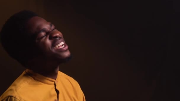 Sarı tişörtlü şık Afro-Amerikan bir adam duygusal olarak elleriyle bir şarkı ve jest söylüyor. Siyah şarkıcı duman ve ışıklarla dolu karanlık bir stüdyoda canlı performans sergiliyor. Kapat.. — Stok video