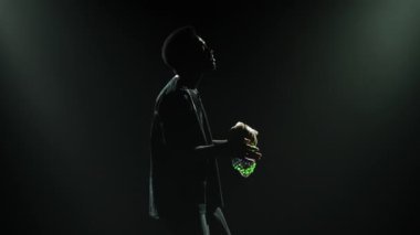 Mutlu siyah adam, çıngırak sesi çıkaran bir Afrika ritim enstrümanı çalmayı seviyor. Parlak enstrüman boncukları stüdyo ışıklarında siyah arka planda parlıyor. Afrika folkloru.