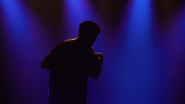 Musique ethnique africaine. Silhouette d'un musicien afro-américain se tape sur le tambour de yuka africain parlant et danse dans un studio sombre sur un fond de lumières bleues. — Video