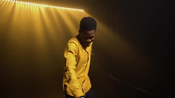 Sarı tişörtlü şık Afro-Amerikan bir adam duygusal olarak elleriyle bir şarkı ve jest söylüyor. Siyah şarkıcı duman ve ışıklarla dolu karanlık bir stüdyoda canlı performans sergiliyor.. — Stok video