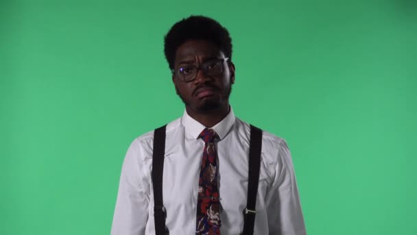 Porträtt av en ung afroamerikan som tittar på kameran, lyssnar uppmärksamt och nickar med huvudet. Svart hane med slips och glasögon i vit skjorta poserar på grön skärm i studio. Närbild. — Stockvideo