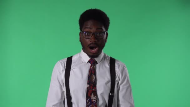 Portrait of young African American man looking at camera with wow surprised expression. Black male with tie and glasses in white shirt posing on green screen in studio. Close up. — Stock Video