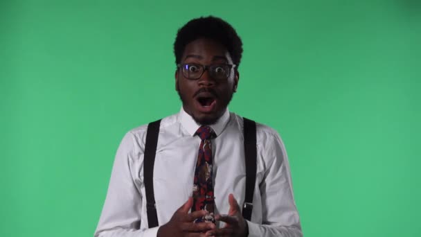 Retrato del joven afroamericano mirando a la cámara con una expresión sorprendida y entusiasta. Hombre negro con corbata y gafas en camisa blanca posando en pantalla verde en el estudio. De cerca.. — Vídeos de Stock