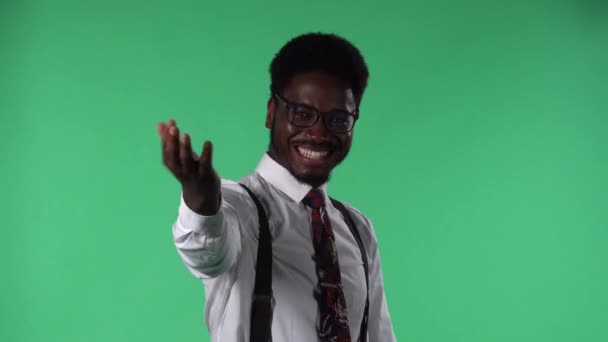 Portrét mladého Afroameričana, jak se dívá do kamery, usmívá se, mává zdravím a gesty přichází sem. Černoch s kravatou a brýlemi v bílé košili pózující na zelené obrazovce ve studiu. Zavřít. — Stock video