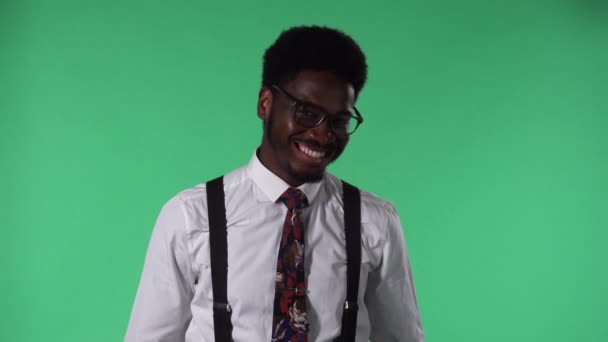 Porträtt av ung afroamerikan som tittar på kameran, ler och flirtar. Svart hane med slips och glasögon i vit skjorta poserar på grön skärm i studio. Närbild. — Stockvideo
