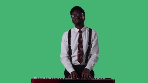 Ritratto di giovane afroamericano che sorride e suona lenta melodia su un sintetizzatore di tastiera. Maschio nero con cravatta e occhiali in camicia bianca in posa sullo schermo verde in studio. Da vicino.. — Video Stock