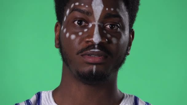 Portrait young African American man looking at camera, reporting and telling lot of interesting information. Black male with an ethnic white pattern on face posing on green screen in studio. Close up. — Stock Video