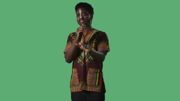 Mikrofona şarkı söyleyen genç Afrikalı Amerikalı adam portresi. Yüzünde etnik beyaz desenli, parlak gömlekli, stüdyoda yeşil ekrana poz veren siyah bir erkek.. — Stok video