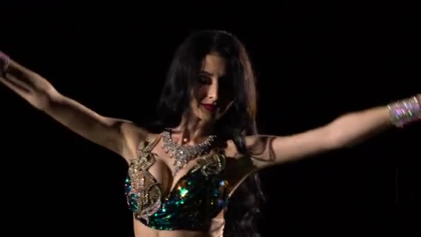 Μια ελκυστική χορεύτρια κουνάει τους γοφούς της με ένα λαμπερό ανατολίτικο ντύσιμο ανάμεσα στις σταγόνες της βροχής. Μπρουνέτ με μακριά μαλλιά που χορεύουν ανατολίτικο χορό σε μαύρο φόντο στούντιο, κοντινό πλάνο. — Αρχείο Βίντεο