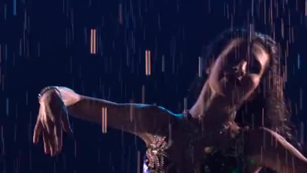 Silhouette of oriental beauty dancing belly dance and moving hips in rain in dark studio. Woman with an attractive body dances and waves her hair in multitude of splashes. Close up. Slow motion. — Stock Video