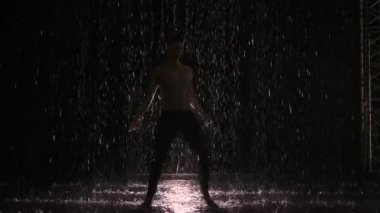 Islak erkek dansçı silueti yağmurda ve su sıçratarak modern bale gösterisi yapıyor. Erkek şehvetli modern koreografi, ışık huzmesinin merkezinde siyah arkaplan üzerinde. Yavaş çekim.