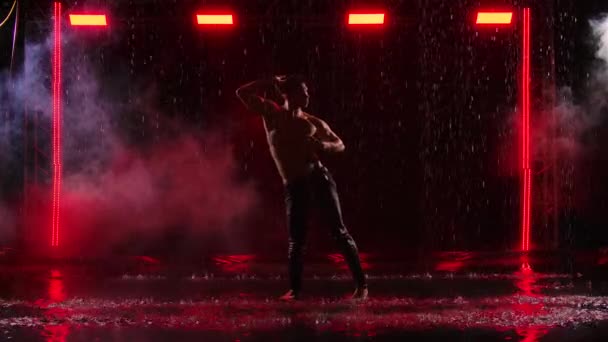 Silhouette Mann mit nacktem Oberkörper führt Choreographie des modernen Balletts im Regen auf schwarzem Hintergrund mit rotem Licht. Nasse männliche Tänzer sorgen beim Tanzen für jede Menge Spritzer. Zeitlupe. — Stockvideo