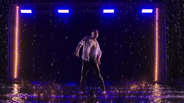 Emotionale Aufführung zeitgenössischer Ballettchoreographien im Regen in dunklem Studio mit blauem Licht. Silhouette eines nassen Mannes, der sich anmutig bewegt und akrobatische Elemente vorführt. Zeitlupe. — Stockvideo