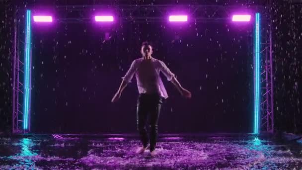 Emotionale Aufführung zeitgenössischer Ballettchoreographien im Regen im dunklen Studio mit violettem Licht. Silhouette eines nassen Mannes, der sich anmutig bewegt und akrobatische Elemente vorführt. Zeitlupe. — Stockvideo