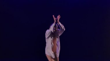 Beyaz gömlekli kadın yağmurda modern balenin dramatik danslarını yapıyor. Bale, karanlık stüdyoda mavi ışıkla modern koreografiyi sergileyerek plastiği hareket ettirir. Ağır çekim. Kapat..