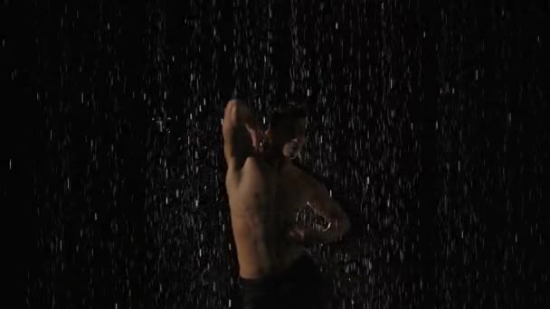 Silhouet van natte mannelijke danser die moderne ballet dans uitvoert in regen en spetterend water. Mannelijke sensuele moderne choreografie op zwarte achtergrond in het centrum van lichtstraal. Langzame beweging. Sluiten.. — Stockvideo