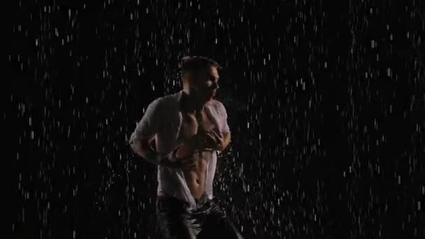 Силуэт мокрого мужчины-танцора, исполняющего современные балетные танцы под дождём и брызгами воды. Мужская чувственная современная хореография на черном фоне в центре светового луча. Медленное движение. Закрыть. — стоковое видео