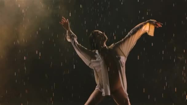 Coreografia de balé sensual contemporânea realizada por bailarina flexível esbelta em meio a gotas de chuva. Mulher molhada em maiô bege dançando romanticamente no estúdio escuro. Silhueta. Movimento lento. Fechar. — Vídeo de Stock