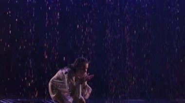 Çağdaş dans balerinleri su yüzeyindeki yağmurda şehvetli bir şekilde dans ederek su sıçratır. Beyaz gömlekli ıslak kadın silueti lacivert ışıkla karanlık stüdyoda plastik gibi hareket ediyor. Ağır çekim. Kapat.