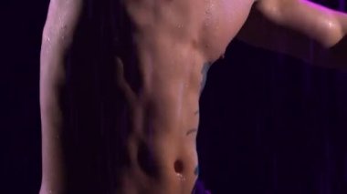 Çağdaş bale, insanoğlu yağmur altında yüzeyde duran modern koreografinin elementlerini sergiliyor. Çıplak vücutlu erkek dansçının şehvetli hareketleri. Siluet. Kapatın. Yavaş çekim.