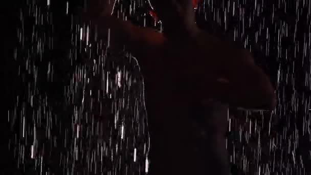 Silhouette de danseur masculin humide exécutant la danse de ballet moderne sous la pluie et éclaboussant l'eau. Chorégraphie moderne sensuelle masculine sur fond noir au centre du faisceau lumineux. Au ralenti. Gros plan. — Video