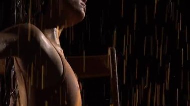 Genç balerin tarafından icra edilen çağdaş balenin duygusal koreografisi. Hafif ıslak kadın, karanlık stüdyoda yağmurun altında sandalyede otururken rahat hareket eder. Siluet. Kapatın. Yavaş çekim.