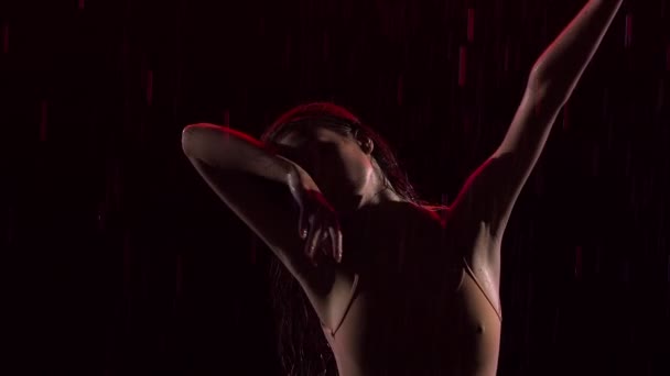 Coreografia de balé sensual contemporânea realizada por bailarina flexível esbelta em meio às gotas de chuva. Silhueta de mulher molhada dançando romanticamente em estúdio escuro com luz vermelha. Fecha. Movimento lento — Vídeo de Stock