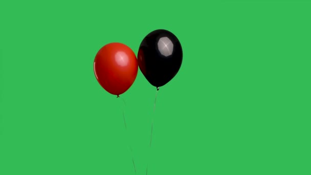 红色和黑色的气球在空气中悬挂在绿色屏幕色键的背景上.用彩带把色彩艳丽的氦气气球包起来.生日，派对装饰，假期，惊喜，礼物慢动作. — 图库视频影像