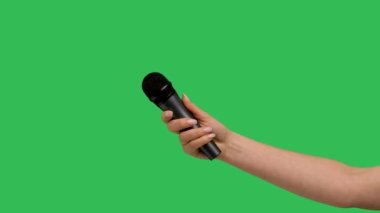 Female hand holding microphone against background green screen chroma key. Close up mic, interview, live press conference, karaoke, singer performance. Slow motion.