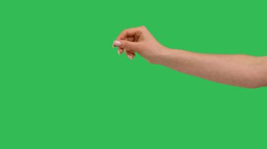 Close up side view of beautiful outstretched female hand with a sprinkling gesture isolated on green screen chroma key background. Chef hand adds pinch salt or spice to the dish. Slow motion.