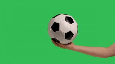 Female hand holds a football classic white black ball on the palm, isolated on green screen chroma key background. Sport play football healthy lifestyle concept. Slow motion. Close up.