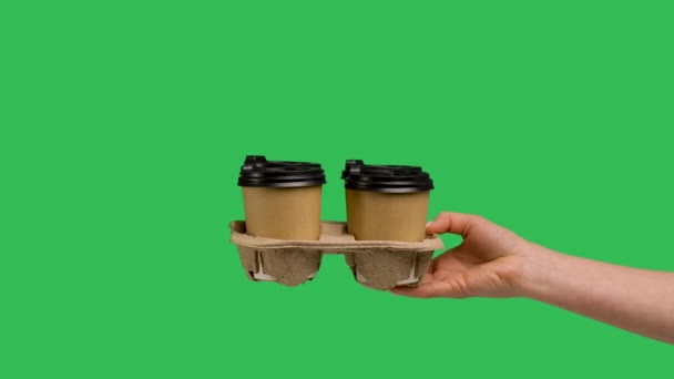 Female hand gives set of paper cups with hot coffee or tea. Close up of paper cups with coffee from barista isolated on green screen chroma key. Food and drink delivery service concept. Slow motion. — стоковое видео