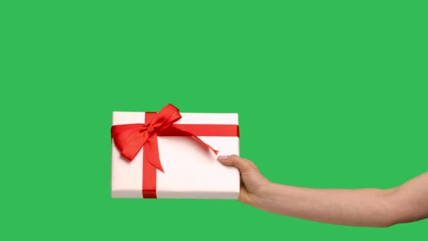 Weibliche Hände, die eine Geschenkschachtel auf dem Hintergrund eines grünen Bildschirmschlüssels geben. Geschenk mit einer schönen roten Schleife für Weihnachten, Neujahr oder Geburtstag aus nächster Nähe. Zeitlupe. — Stockvideo