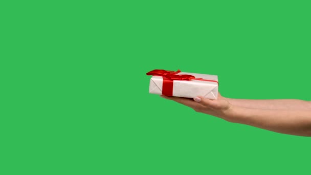 Женские руки дарят подарочную коробку на фоне зеленого экрана хроматического ключа. подарок с красивым красным бантом на Рождество, Новый год или день рождения крупным планом. замедленное движение. — стоковое видео