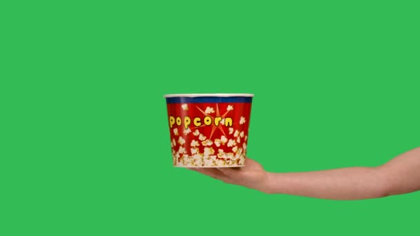 Female hands giving a bucket of popcorn close up. Woman points to the box and makes a thumbs up gesture. A container with a delicious snack on the background of a green screen chroma key. Slow motion. — 图库视频影像
